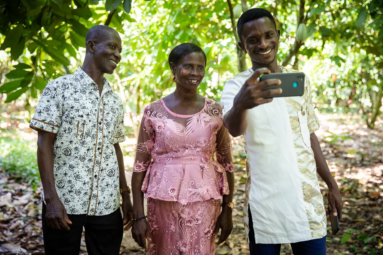George_Ansah_(left),_Mina_Antwiwaa_(middle)_and_Bismark_Domena_(right),_all_cocoa_farmers,_take_a_selfie_photo_in_Abakoase,_Fanteakwa,_Eastern_Region_of_Ghana._November_12,_2021.
